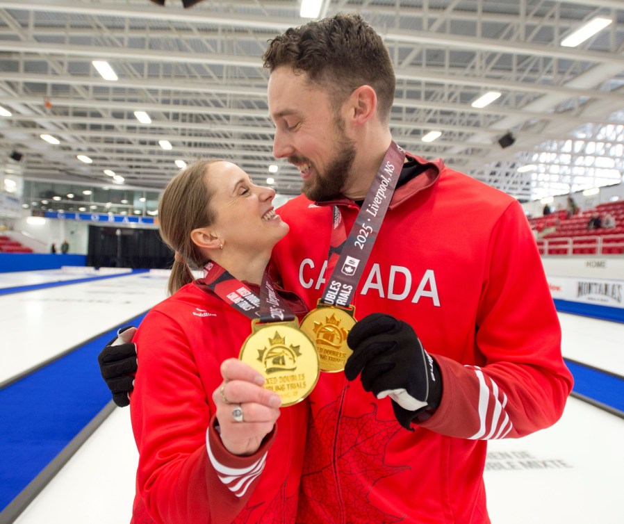 Brett Gallant and Jocelyn Peterman smile at each other while wearing gold medals and red jackets