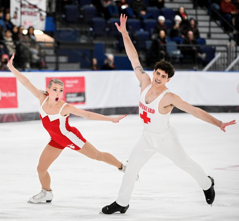 Piper Gilles in a red swimsuit-like costume and Paul Poirier in a white tank top and pants