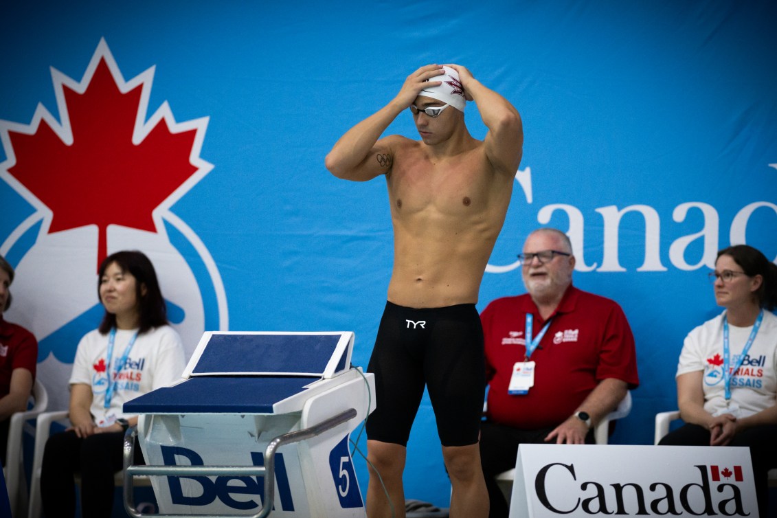 Ilya Kharun adjusts his swim cap while standing on the deck