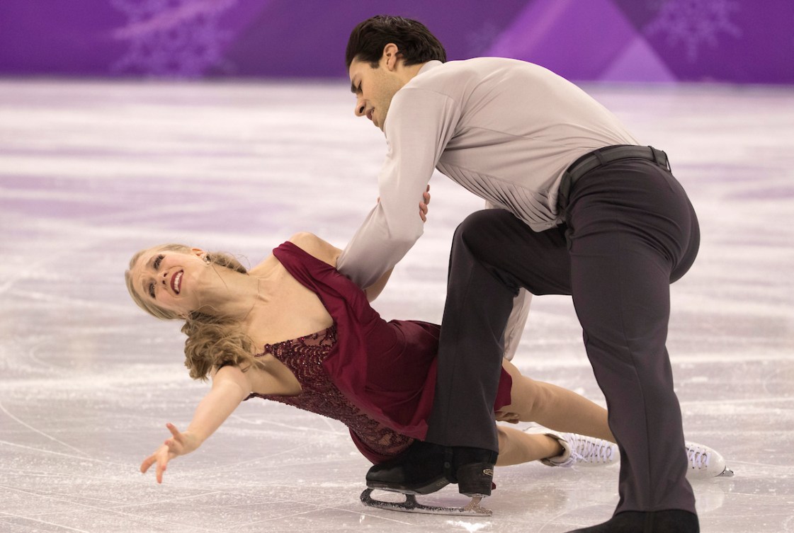 Kaitlyn Weaver in a red dress does a hydroblade move with  partner Andrew Poje dressed in a grey shirt and black pants