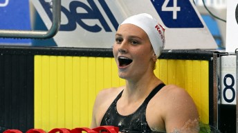 Summer McIntosh wearing a white cap and black suit smiles at the end of the pool
