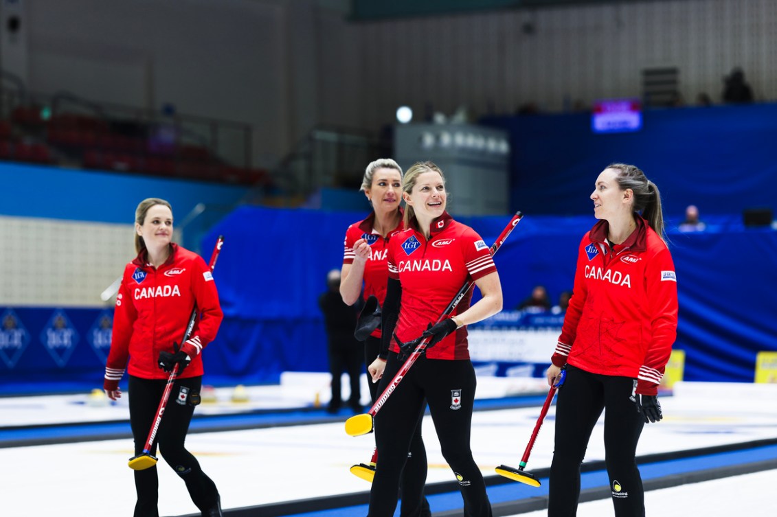 Four women curlers in red jackets and black pants walk down a sheet of ice