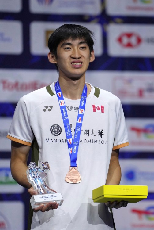Victor Lai in a white shirt stands on the podium wearing a bronze medal