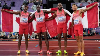 Canada's 4x100m relay team poses with Canadian flags held behind them