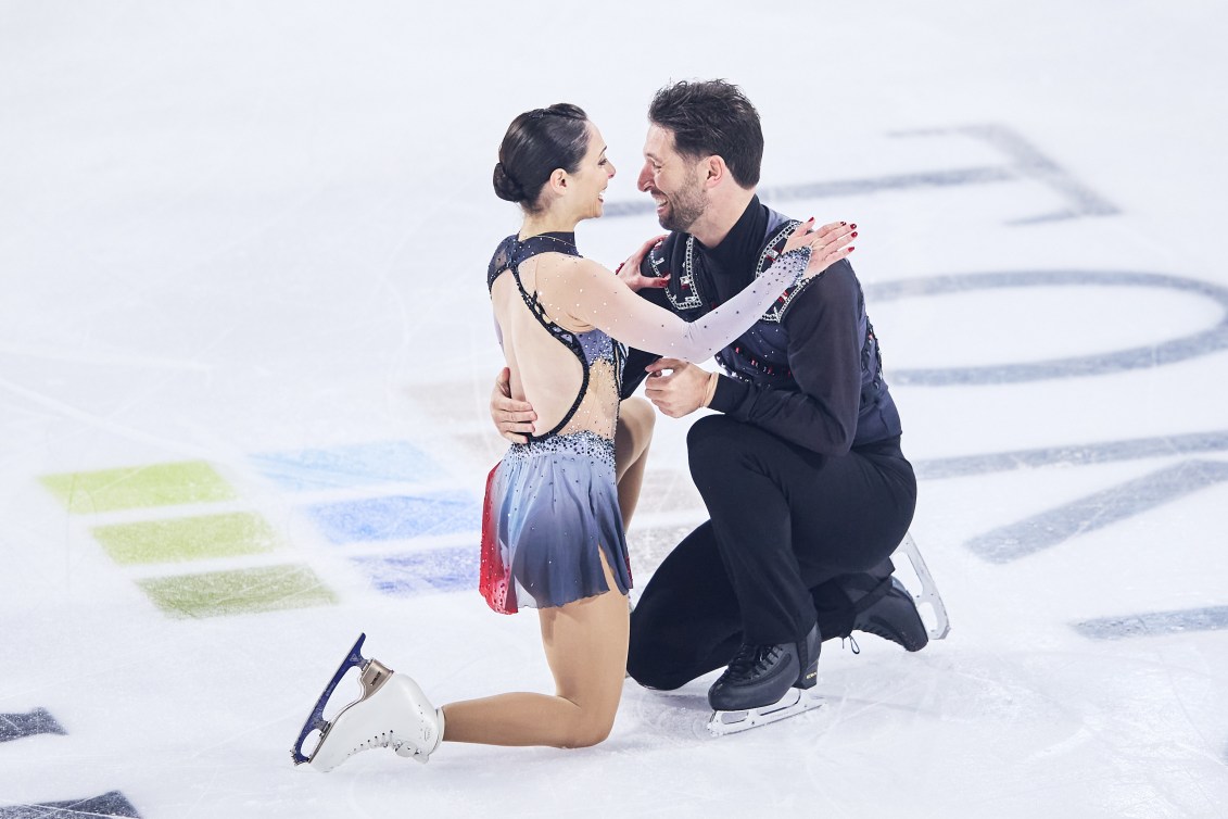 Deanna Stellato-Dudek in a grey dress and Maxime Deschamps in black pants and top kneel on the ice at the end of the program 