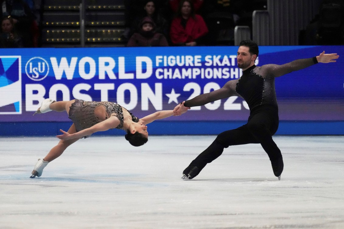 Female skater in grey dress, male skater in black top and pants perform a death spiral on ice 
