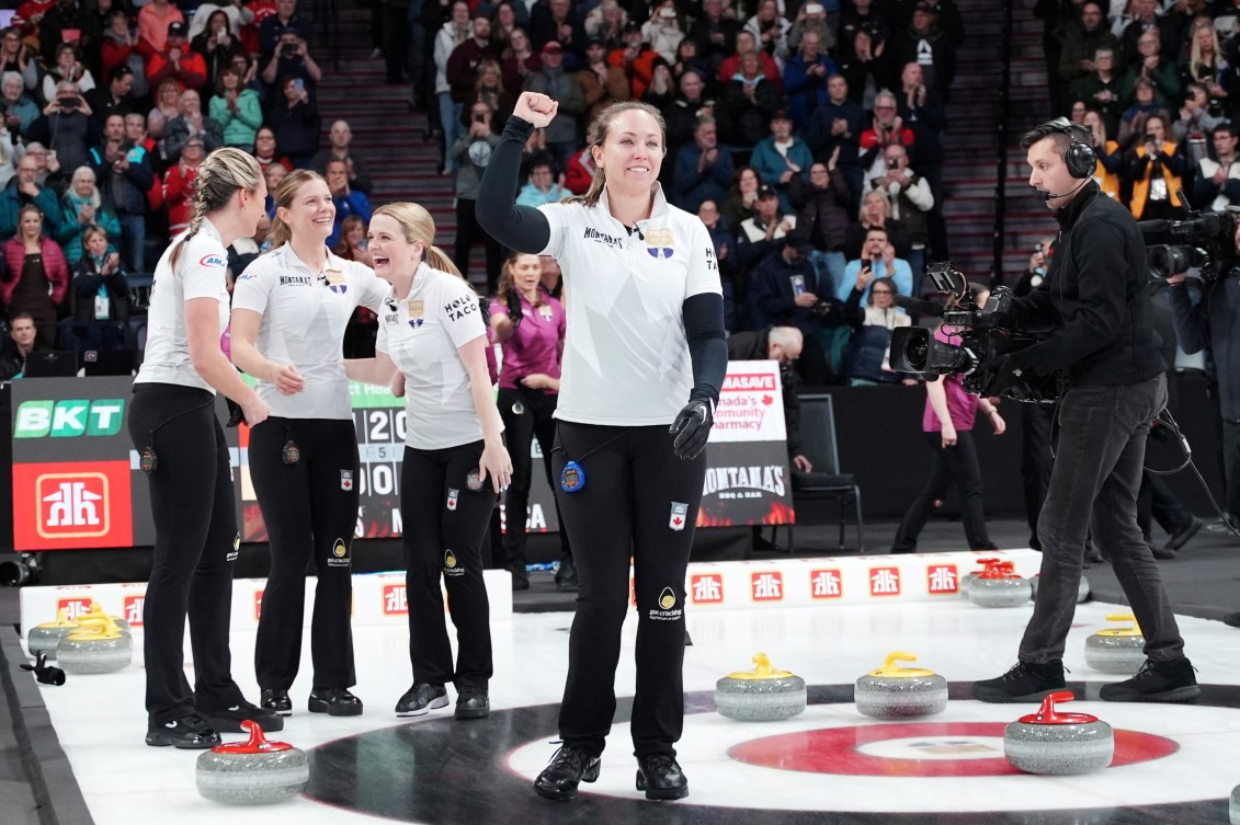 Rachel Homan in white shirt and black pants pumps her first towards the crowd while her teammates laugh with each other behind her