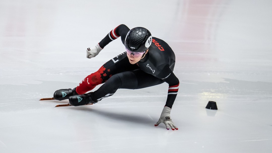 Female short track speed skater in black and red skin suit goes around a turn on the ice