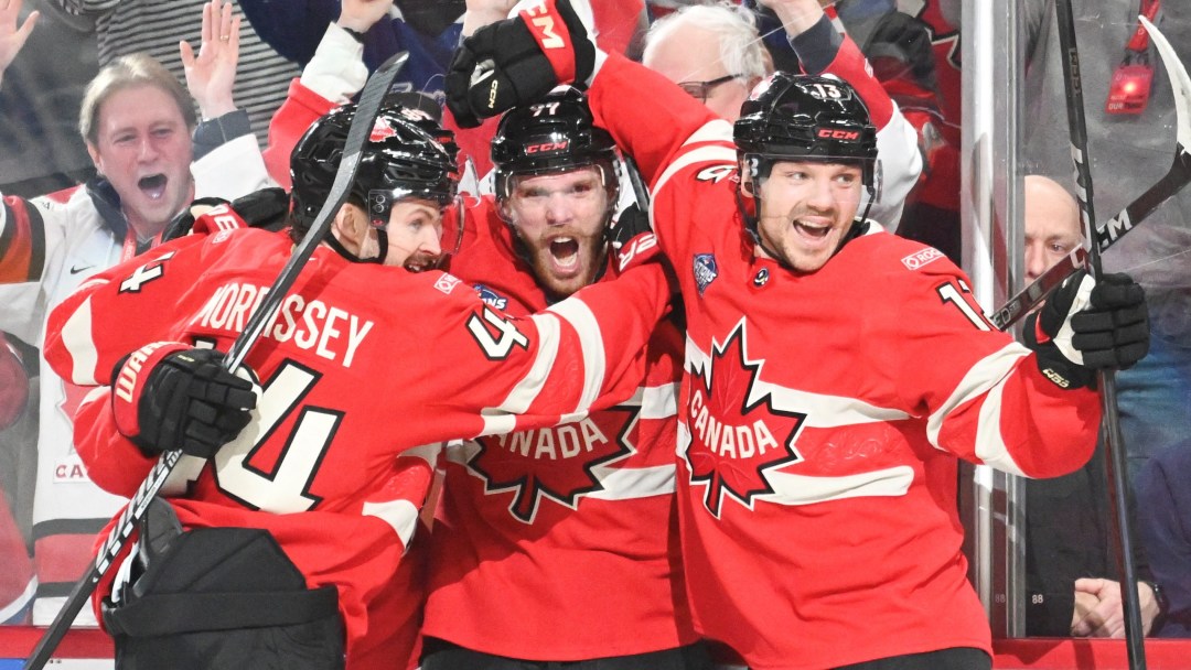Three players in red Canada jerseys celebrate against the glass