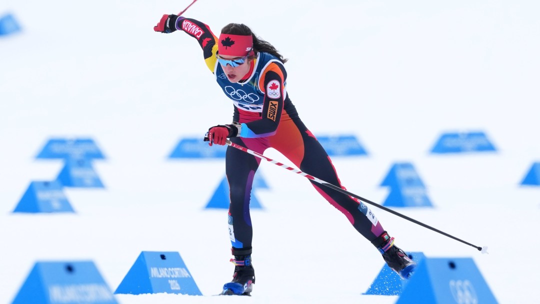 Alison MacKie of Canada races during the women’s 10km interval start free in cross-country skiing at the Milano Cortina 2026 Winter Olympics in Tesero, Italy, skiing along the course with poles planted and snow spraying behind her.