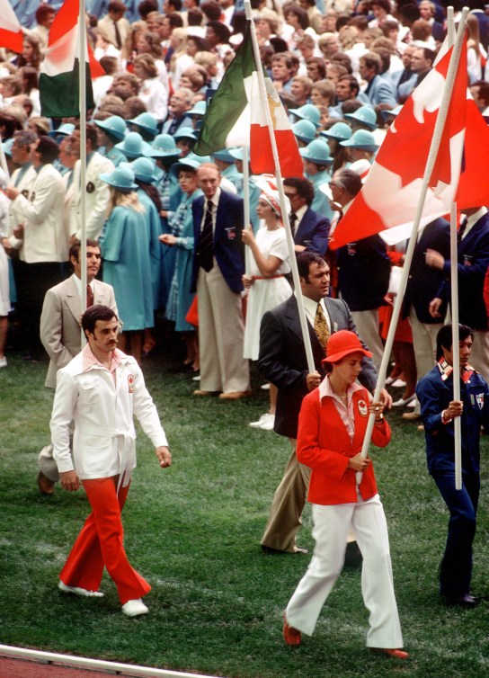 Abby Hoffman dressed in red jacket and white pants carries the Canadian flag