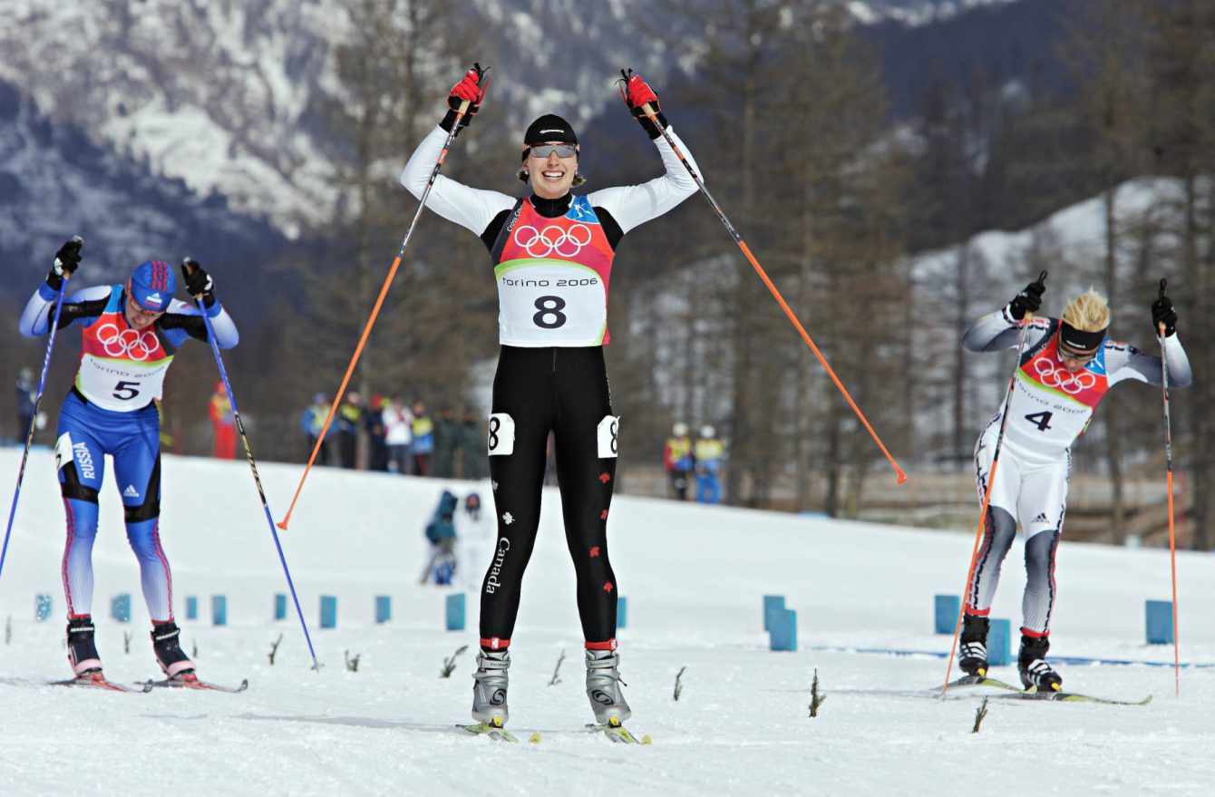 Chandra Crawford (8), de Canmore (Alberta), lève les bras pour célébrer tandis qu’elle franchit la ligne d’arrivée et remporte la médaille d’or à l’épreuve féminine de sprint en ski de fond aux Jeux olympiques de Turin 2006 à Pragelato Plan (Italie) le mercredi 22 février 2006. L’Allemande Claudia Kuenzel (4), médaillée d’argent, et la Russe Alena Sidko (5), médaillée de bronze, ne sont pas loin derrière. (PHOTO PC/Frank Gunn)
