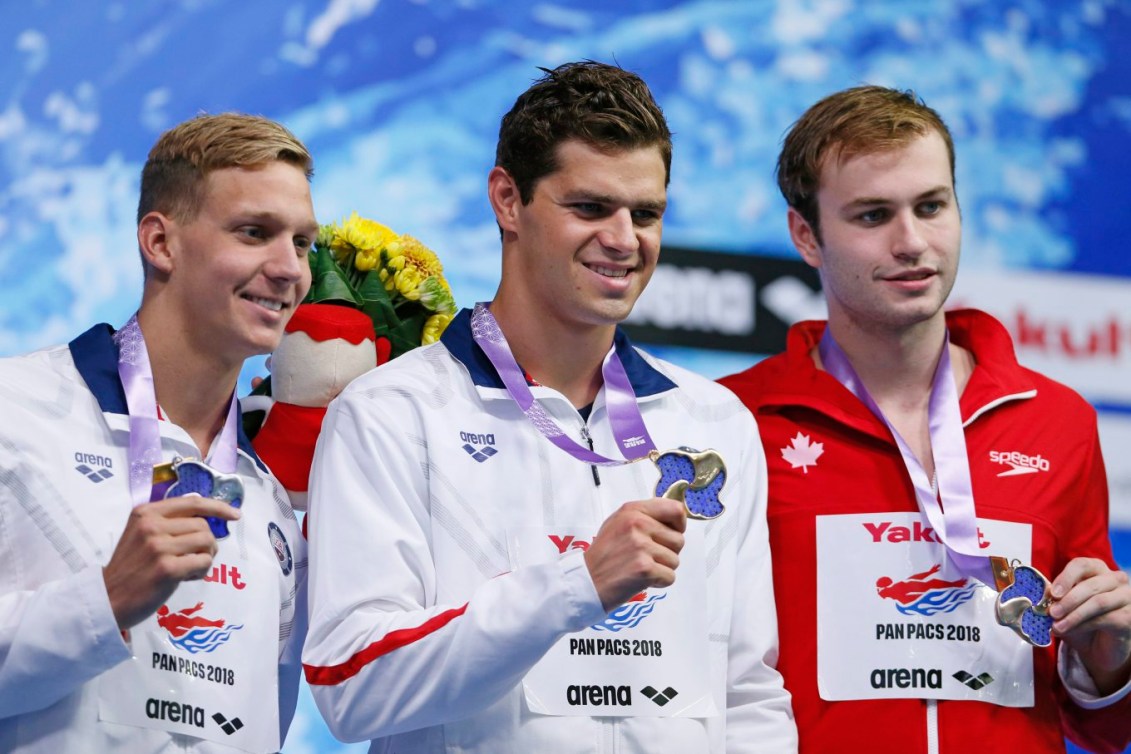 De gauche à droite : le médaillé d'argent Caeleb Dressel, des États-Unis, le médaillé d'or Michael Andrew, des États-Unis, et le médaillé de bronze canadien Yuri Kisil, aux Championnats pan-pacifiques à Tokyo, le 12 août 2018. AP Photo/Koji Sasahara