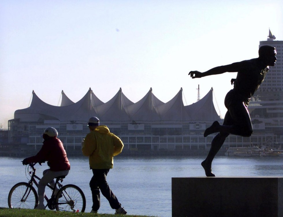 Un cycliste et un joggeur parcourent la digue du parc Stanley à Vancouver devant la statue de Harry Jerome.